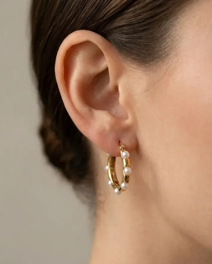 Side profile of a model wearing a small gold and pearl huggie earring.
