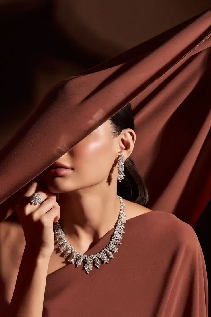 A model partly veiled in rust silk wearing a diamond necklace and drop earrings.