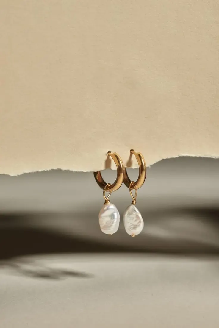 Gold hoop earrings with baroque pearl drops on a pale sand-coloured set.