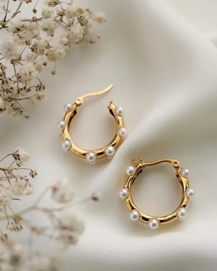 Gold hoops with pearls on cream linen beside dried gypsophila.