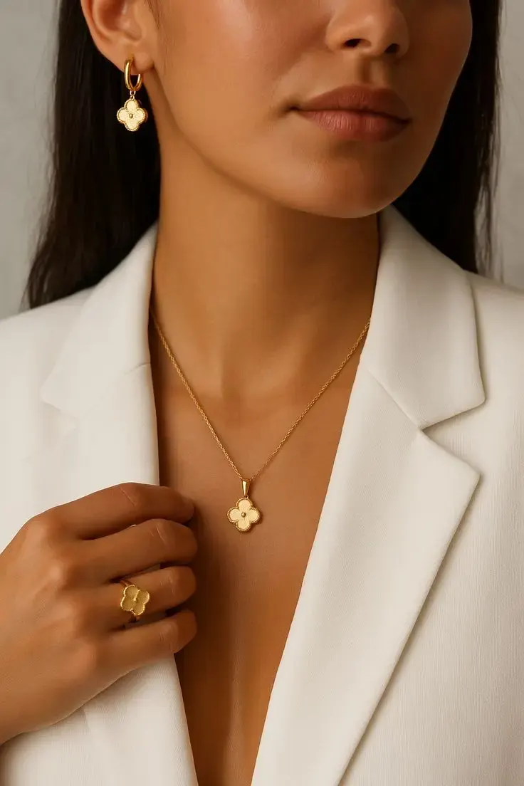 A model in a white blazer wearing a gold clover pendant and ring.