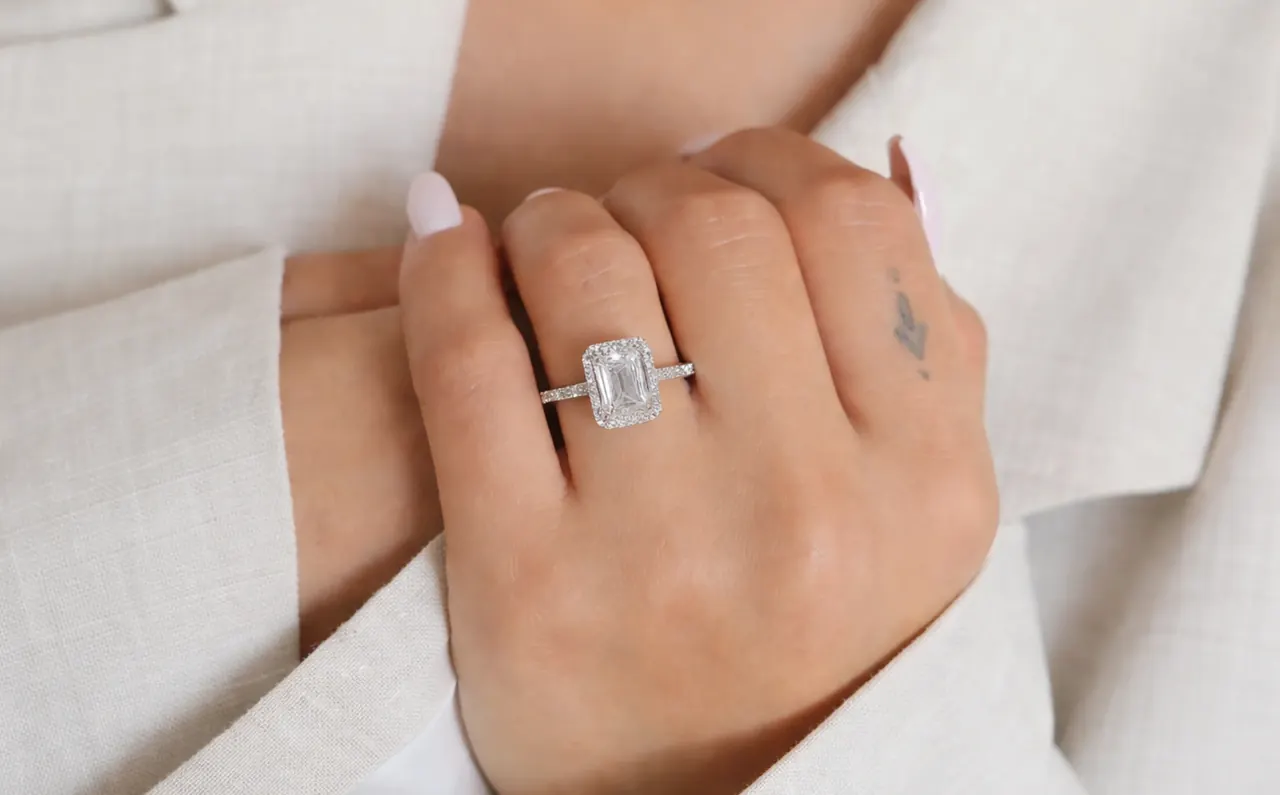 A hand in a white linen sleeve wearing an emerald-cut diamond solitaire.